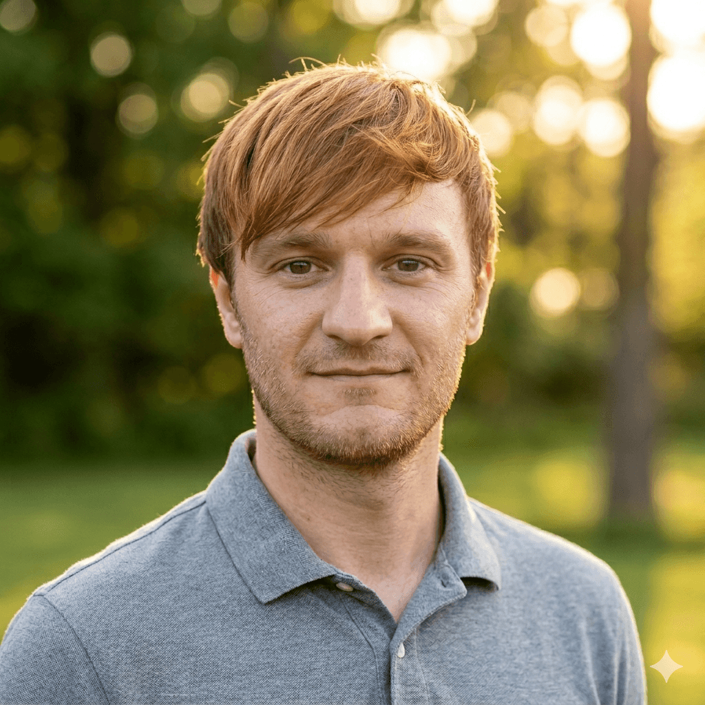 Man with reddish hair and stubble wearing a grey polo shirt in sunny outdoor light.
